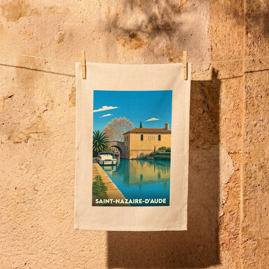 Torchon souvenir de la ville de Saint-Nazaire-d'Aude avec une illustration stylisée d'un canal et d'une bâtisse ensoleillée.