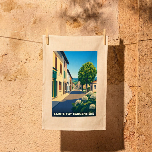 Torchon souvenir de la ville de Sainte-Foy-l'Argentière avec une illustration stylisée d'une rue ensoleillée.