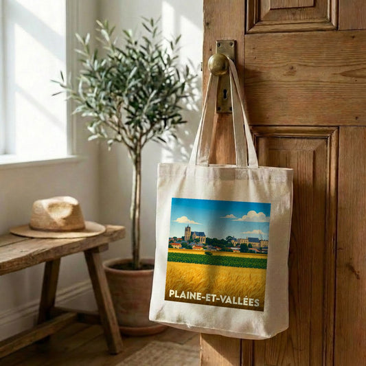 Tote bag souvenir de la ville de Plaine-et-Vallées avec une illustration stylisée de champs et du village.